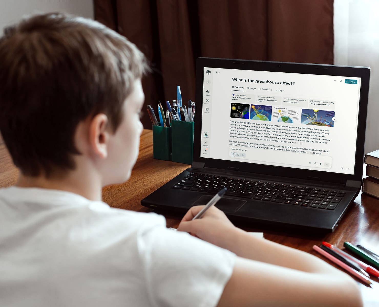 Student at a desk with laptop open showing a Perplexity-style chat saying: What is the greenhouse effect?