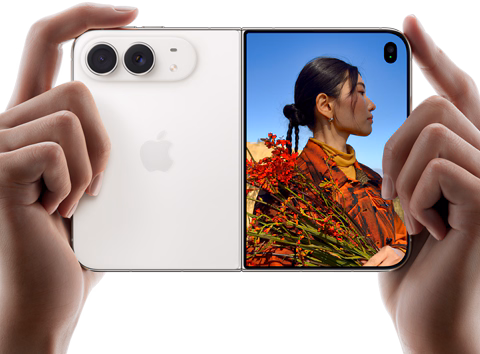 iPhone Duo, couleur blanc stellaire, deux mains le tiennent en orientation horizontale, déplié, le volet gauche montre les deux caméras arrière Fusion 48 mégapixels, le volet droit montre l’écran externe affichant une personne en train de se faire photographier, qui peut se voir pendant la prise grâce à Duo Preview