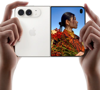iPhone Duo, couleur blanc stellaire, deux mains le tiennent en orientation horizontale, déplié, le volet gauche montre les deux caméras arrière Fusion 48 mégapixels, le volet droit montre l’écran externe affichant une personne en train de se faire photographier, qui peut se voir pendant la prise grâce à Duo Preview